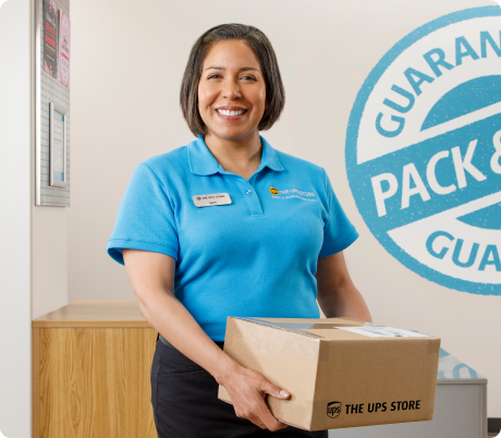 A woman standing at a counter, holding a package at The UPS Store.